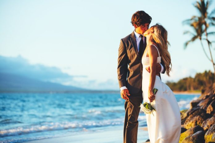 Picture of a bridge & groom kissing on the beach. Find out the best Hawaiian resorts for a wedding.